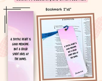 May include: A bookmark with a pink and white gradient design, featuring the text "A JOYFUL HEART IS GOOD MEDICINE. BUT A CRUSH SPIRIT DRIES UP THE BONES." and "Proverbs 17:22." The bookmark is 2 inches by 6 inches.