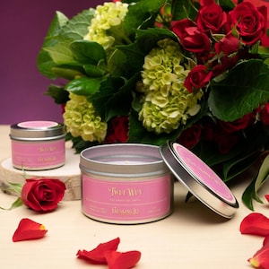 May include: Two pink and silver candles with the text "Two Way" and "Dreaming Of" on the labels. The candles are surrounded by red rose petals and a bouquet of red roses.