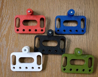 May include: Five colorful, rectangular, 3D-printed objects with a textured surface. Each has a central opening, two side openings, and a small, cylindrical knob. Colors include red, blue, black, white, and green.