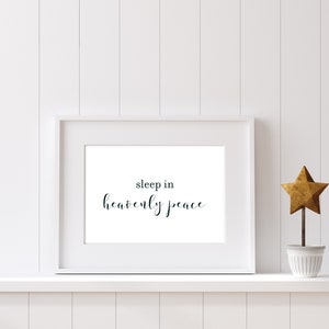 Puede incluir: Impresión enmarcada en blanco con el texto "sleep in heavenly peace" en fuente cursiva negra. La impresión está en un estante blanco con un adorno de estrella dorada en una maceta blanca.
