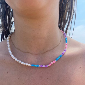 May include: A layered necklace with a strand of white pearls and a strand of colorful beads. The beads are pink, purple, blue, and turquoise.