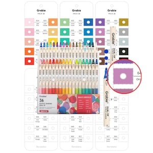 Op de afbeelding: Een set van 36 Grabie acrylmarkers met dubbele punt in een rechthoekige doos met een kleurrijk cirkelpatroon. De markers staan in een rij en hebben elk een crèmekleurige huls. Drie genummerde kleurkaarten zijn inbegrepen.