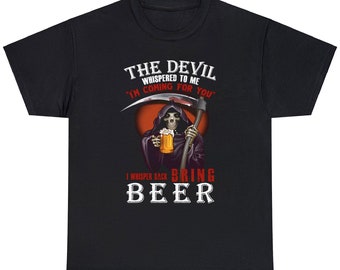 以下が含まれることがあります： 黒いTシャツ。死神がビールジョッキと鎌を持ったグラフィック。テキストは「THE DEVIL WHISPERED TO ME 'I'M COMING FOR YOU' I WHISPER BACK BRING BEER」と書かれています。デザインは赤とオレンジの背景です。