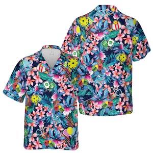 Può includere: Due camicie a maniche corte, abbottonate, di colore blu navy con una stampa tropicale che presenta fiori, foglie e disegni colorati di paddleball.