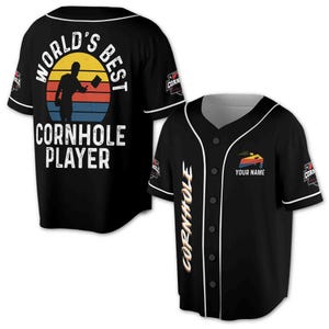 Könnte beinhalten: Schwarzes Baseball-Trikot mit weißem Besatz. Es zeigt den Text "WORLD'S BEST CORNHOLE PLAYER" und eine Silhouette eines Spielers, der einen Beutel vor einem Sonnenuntergang wirft. Es hat auch den Text "CORNHOLE" und einen anpassbaren Namensbereich.