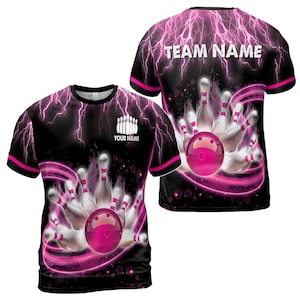 May include: Black and pink bowling shirt with a graphic of bowling pins and a ball. The back of the shirt says "TEAM NAME". The front of the shirt says "YOUR NAME".