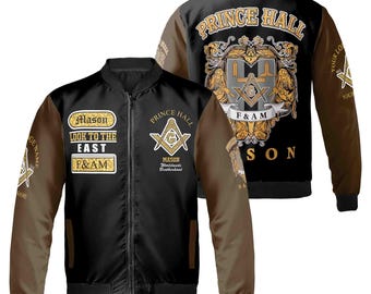 Puede incluir: Chaqueta bomber negra y marrón con un símbolo masónico dorado y el texto "Prince Hall" en la espalda. La parte delantera de la chaqueta tiene un parche dorado con el texto "Mason Look to the East F&AM".