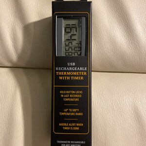 May include: Black and silver USB rechargeable thermometer with a digital display and a timer. The thermometer has a temperature range of -40°F to 500°F and an audible alert when the timer is done.