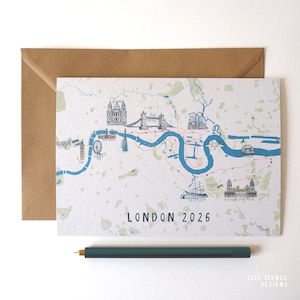 Puede incluir: Una tarjeta blanca con un mapa de Londres, con puntos de referencia como el London Eye y el Tower Bridge, con el texto "LONDON 2026". Un sobre marrón y un bolígrafo verde también son visibles.