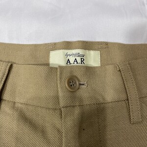 Puede incluir: Primer plano de un pantal&oacute;n beige con cierre de bot&oacute;n y una etiqueta que dice "A.A.R. Urban". La tela tiene un tejido texturizado. El pantal&oacute;n probablemente forma parte de una colecci&oacute;n de ropa.