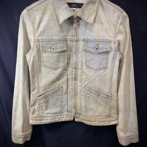 May include: A light-wash blue denim jacket featuring a full-length front zipper, a pointed collar, and long sleeves. The garment includes two chest pockets with buttoned flaps and two lower slanted pockets. The interior label reads INED Made in Japan.