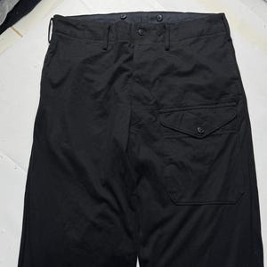 Puede incluir: Pantalones negros con cierre de bot&oacute;n y un solo bolsillo en la pierna derecha. Los pantalones tienen un dise&ntilde;o de pierna recta y un estilo cl&aacute;sico y minimalista. La tela parece ser de peso medio.