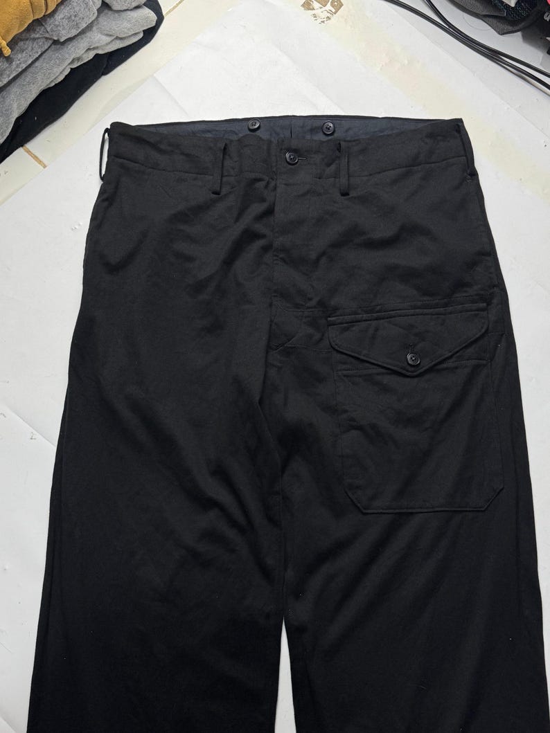 Puede incluir: Pantalones negros con cierre de bot&oacute;n y un solo bolsillo en la pierna derecha. Los pantalones tienen un dise&ntilde;o de pierna recta y un estilo cl&aacute;sico y minimalista. La tela parece ser de peso medio.