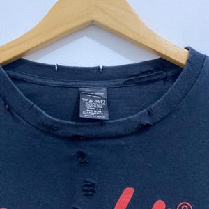 May include: A black t-shirt with a distressed, frayed neckline and small holes throughout the fabric. The shirt features a red graphic print and a black interior tag that reads NUMBER (N)INE 100% COTTON, size 4, and MADE IN JAPAN.