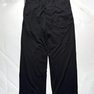 Puede incluir: Pantalones negros de pernera ancha con cierre de bot&oacute;n y un solo bolsillo en la pierna derecha. Los pantalones tienen cintura alta y un corte relajado. La tela parece ser un material ligero.