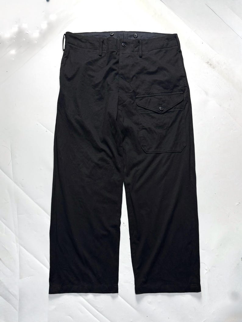 Puede incluir: Pantalones negros de pernera ancha con cierre de bot&oacute;n y un solo bolsillo en la pierna derecha. Los pantalones tienen cintura alta y un corte relajado. La tela parece ser un material ligero.