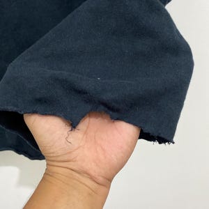 May include: A dark navy blue fabric garment featuring a raw, distressed hemline with visible frayed threads and an uneven, jagged edge along the bottom border of the material, showcasing a textured and worn appearance in the textile construction.