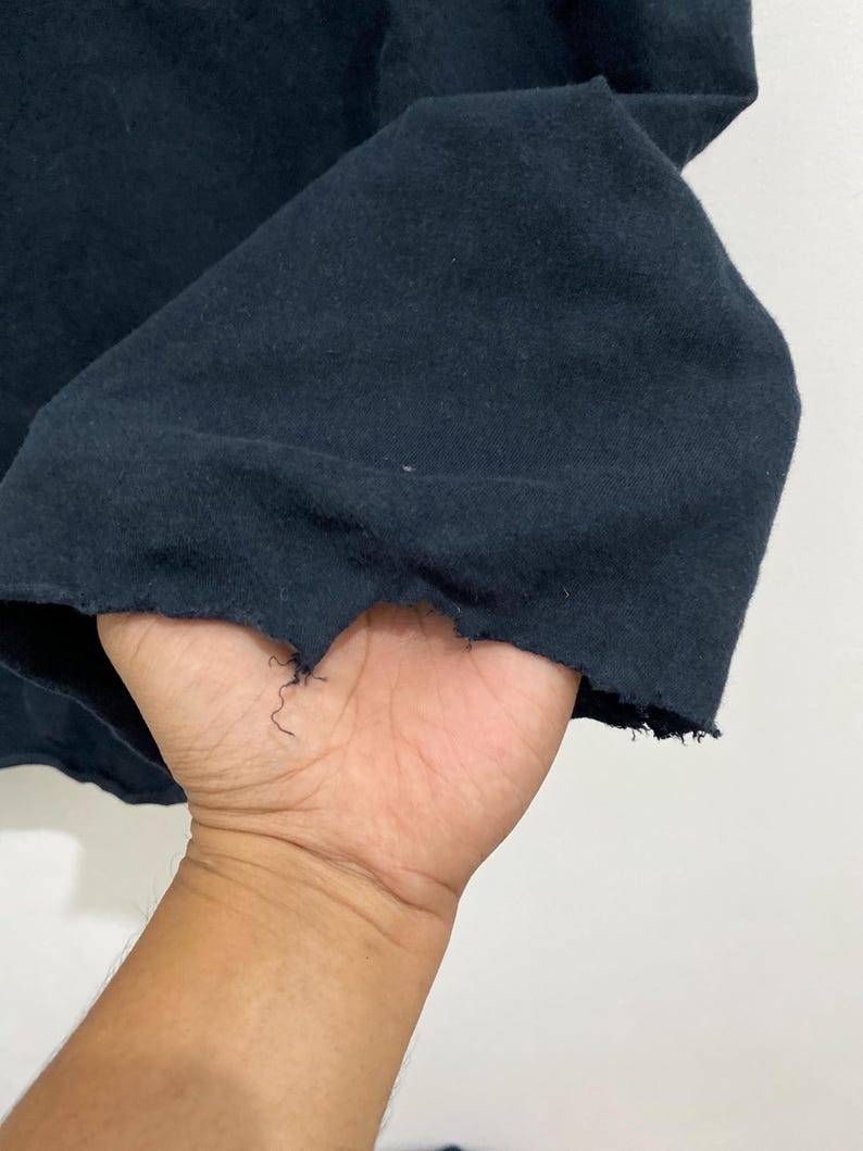 May include: A dark navy blue fabric garment featuring a raw, distressed hemline with visible frayed threads and an uneven, jagged edge along the bottom border of the material, showcasing a textured and worn appearance in the textile construction.