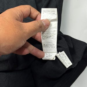 May include: Black t-shirt with a white tag. The tag has the text "HG-T86-084" and "100%" printed on it. The tag also has Japanese text and the number "1060".