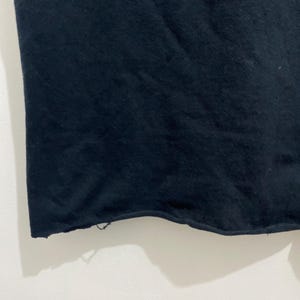 May include: A solid black fabric garment featuring a raw, unfinished hemline along the bottom edge. The material appears to be a soft, opaque textile with a slightly textured surface, showing a clean, straight cut across the width of the piece.