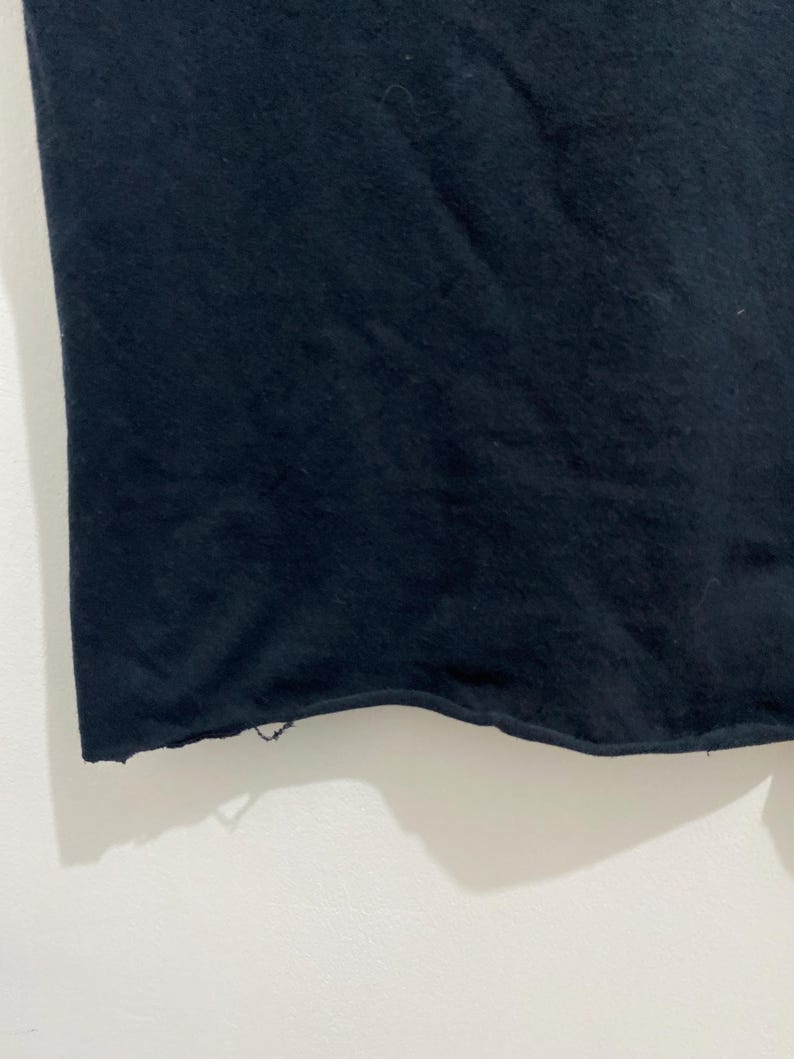 May include: A solid black fabric garment featuring a raw, unfinished hemline along the bottom edge. The material appears to be a soft, opaque textile with a slightly textured surface, showing a clean, straight cut across the width of the piece.