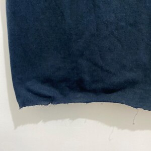 May include: A dark navy blue fabric garment featuring a raw, unfinished hemline. The bottom edge of the material displays a frayed, uneven texture with loose threads hanging from the side, showcasing a simple, unhemmed construction style.