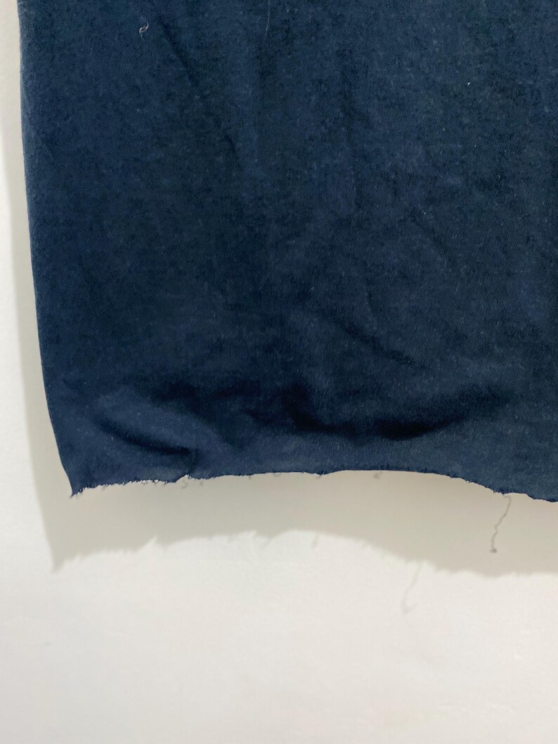 May include: A dark navy blue fabric garment featuring a raw, unfinished hemline. The bottom edge of the material displays a frayed, uneven texture with loose threads hanging from the side, showcasing a simple, unhemmed construction style.