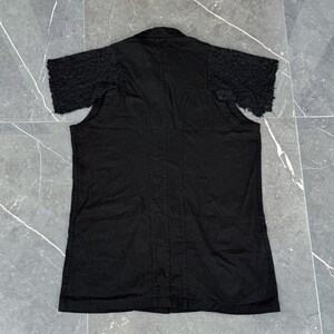 May include: Black short-sleeved shirt with textured sleeves. The shirt has a button-down front and a collar. The sleeves have a unique, textured design. The shirt is made of a dark fabric.