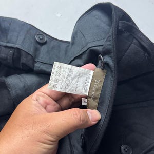 Puede incluir: Pantalones negros con botones. La etiqueta dice "Y's for men", "FABRIQUE AU JAPON" y "MADE IN JAPAN". La tela es 100% algod&oacute;n. Los pantalones tienen una etiqueta con instrucciones de cuidado y el c&oacute;digo MF-P14-028.