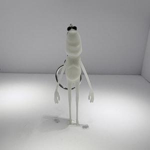 May include: A white frog-shaped keychain with a silver keyring. The frog has long, thin limbs, a rounded body, and small black eyes. The keychain is made of a smooth, possibly plastic material.
