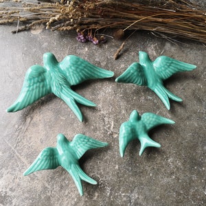 May include: Four teal blue ceramic swallow bird wall decor pieces. The birds are in flight and have detailed wings and tails.
