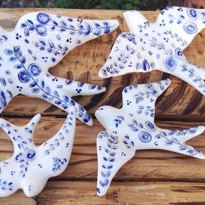 Może przedstawiać: Cztery białe ceramiczne figurki jaskółek z niebieskimi wzorami kwiatowymi. Jaskółki są ułożone w grupie na drewnianej powierzchni.