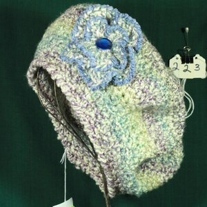 May include: A white crocheted beret with a blue crocheted flower and a blue glass bead in the center. The beret is on a display stand with a price tag that says "223".