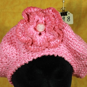 May include: Pink crocheted beret with a large pink crocheted flower on top. The flower has a white button in the center.