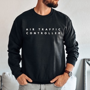 Könnte beinhalten: Ein schwarzer Pullover mit dem Aufdruck "AIR TRAFFIC CONTROLLER" in Weiß auf der Vorderseite.