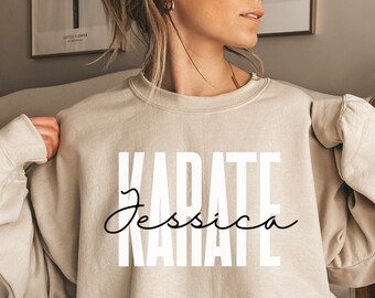 Puede incluir: Una sudadera beige con la palabra "KARATE" impresa en letras blancas y el nombre "Jessica" escrito en cursiva debajo.