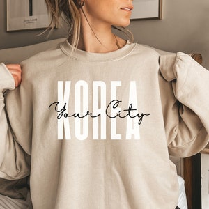 May include: A beige sweatshirt with the text "KOREA Your City" printed in white on the front.
