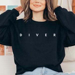 Puede incluir: Una sudadera negra con la palabra "DIVER" impresa en blanco en la parte delantera.