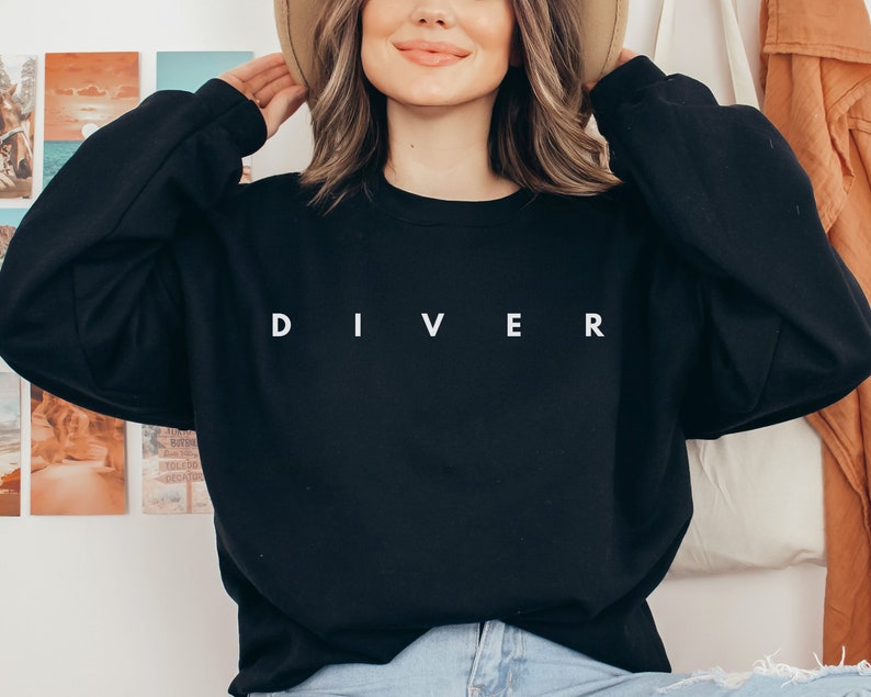 Puede incluir: Una sudadera negra con la palabra "DIVER" impresa en blanco en la parte delantera.