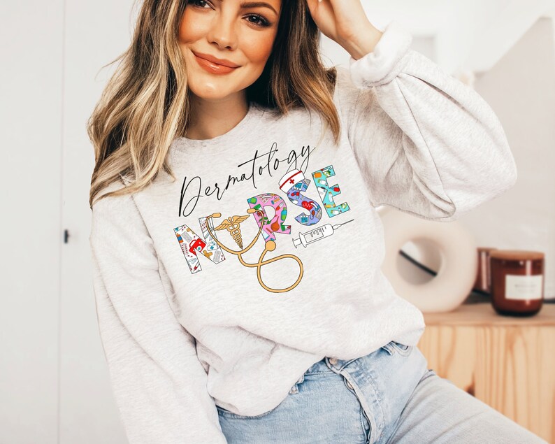 May include: A gray sweatshirt with the text "Dermatology Nurse" in black script. The word "Nurse" is made up of colorful medical symbols and illustrations.