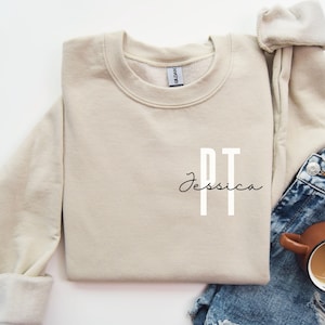 May include: A beige sweatshirt with the letters "PT" and the name "Jessica" printed on the front.