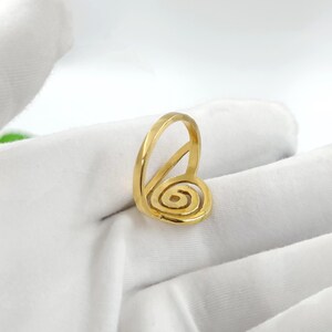 May include: A gold-colored ring with a spiral design. The ring features a rounded band and a spiral element, creating a unique and artistic look. The ring is set against a white background.