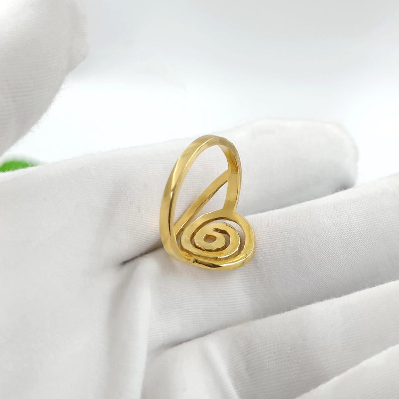May include: A gold-colored ring with a spiral design. The ring features a rounded band and a spiral element, creating a unique and artistic look. The ring is set against a white background.