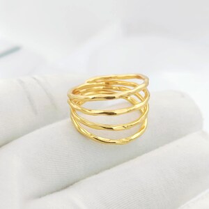 Peut inclure: Une bague dorée avec un design texturé et martelé. La bague comporte cinq bandes empilées, chacune avec une surface inégale. Le bijou est présenté sur un fond blanc.