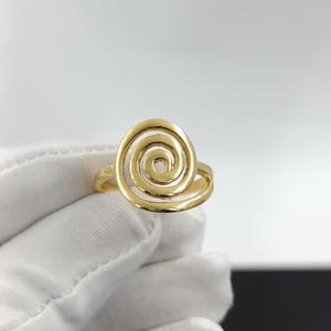 May include: A gold-colored ring featuring a spiral design. The ring's band is smooth, and the spiral is open, creating a unique and eye-catching piece of jewelry. The ring is shown against a white background.