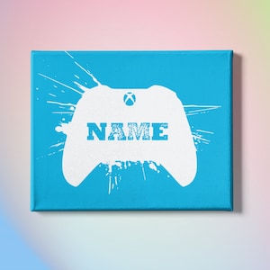 May include: A blue canvas print with a white silhouette of a video game controller with the word "NAME" in the center. The controller is surrounded by white paint splatters.