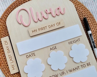 May include: A wooden growth chart with a pink inscription "Olura" at the top. The chart has sections for "My First Day Of", "My Last Day Of", "Date", "Age", "Height", and "When I Grow Up, I Want To Be".