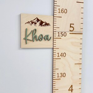 Puede incluir: Un medidor de crecimiento de madera con un dise&ntilde;o de monta&ntilde;a y el nombre "Khoa" en letras verdes. El medidor mide de 110 a 180 pulgadas.