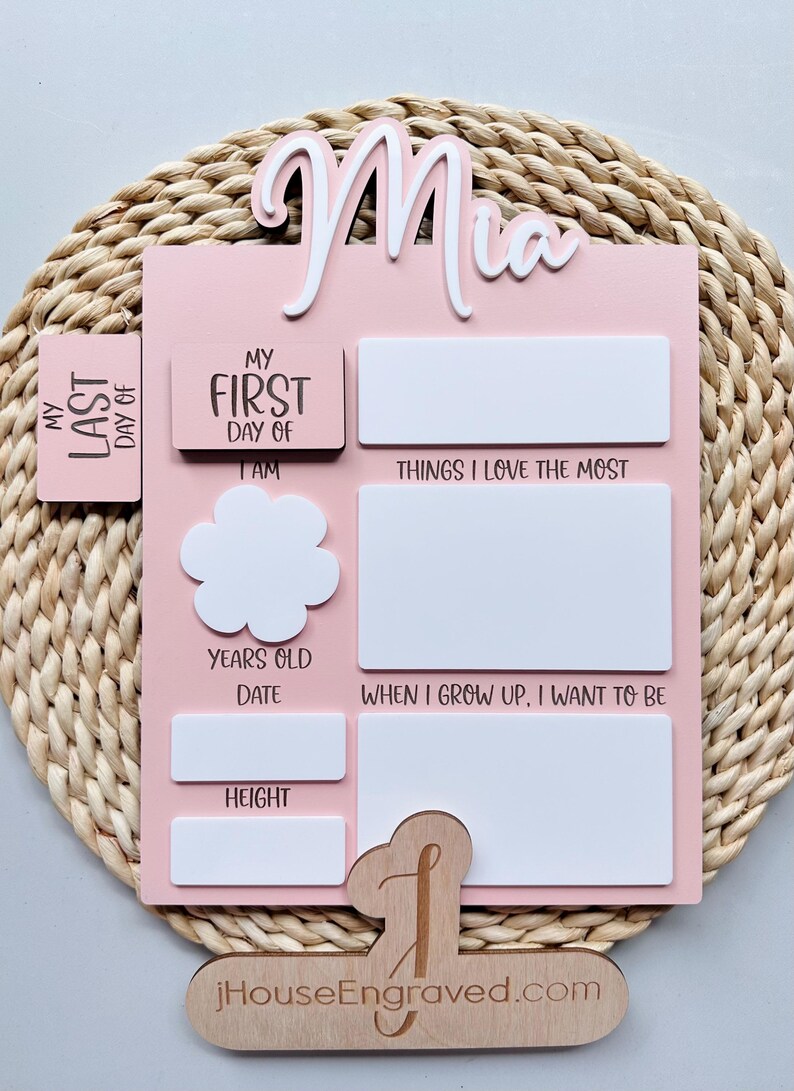 Puede incluir: Un gr&aacute;fico de crecimiento de madera rosa y blanco con el nombre "Mia" en la parte superior. Tiene espacios para rellenar informaci&oacute;n sobre el primer y &uacute;ltimo d&iacute;a del ni&ntilde;o, su edad, su altura y las cosas que le gustan. El gr&aacute;fico est&aacute; sobre una superficie de mimbre tejido.