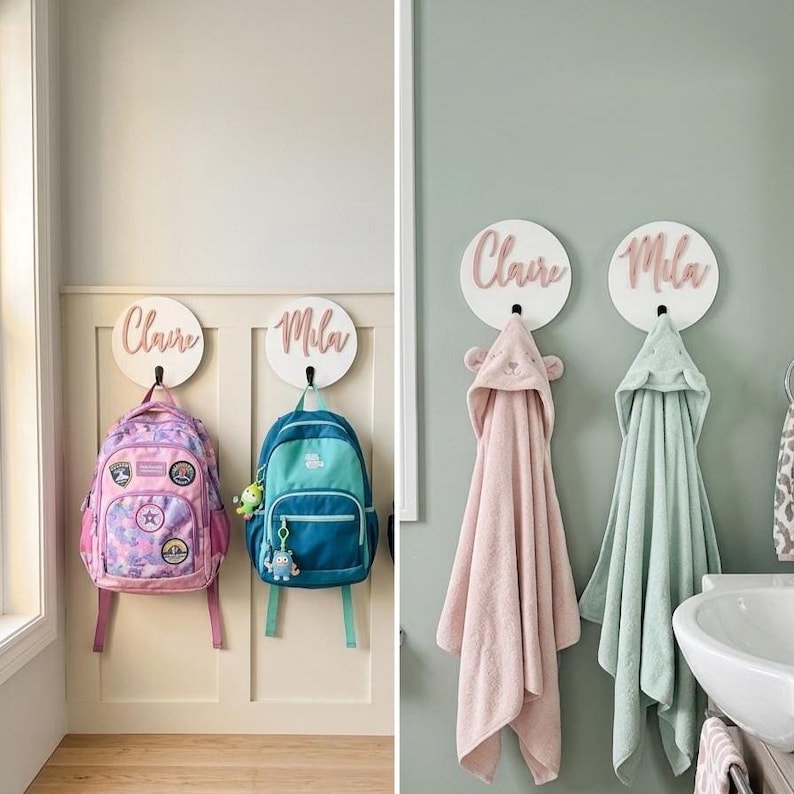 Puede incluir: Cuatro placas circulares blancas montadas en la pared con nombres en relieve escritos en rosa. Dos placas sostienen mochilas coloridas, mientras que las otras dos sostienen toallas con capucha. Los nombres Claire y Mila aparecen en cada placa.
